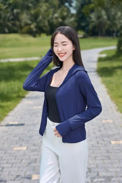 Cô gái mặc áo xanh đứng ngoài trời với mái tóc dài buông tự nhiên.