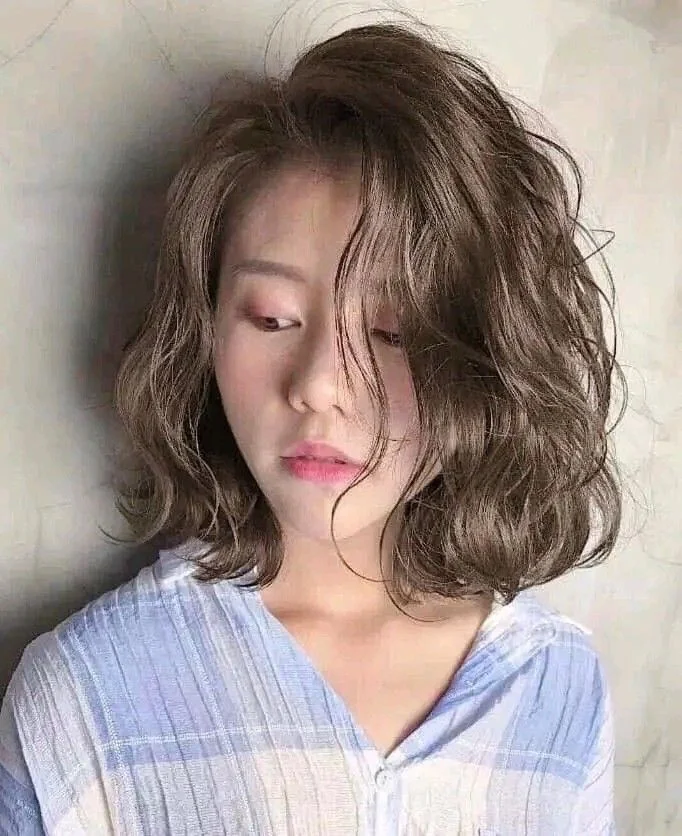 Cô gái với tóc ngang vai màu nâu khói, uốn sóng rối tự nhiên