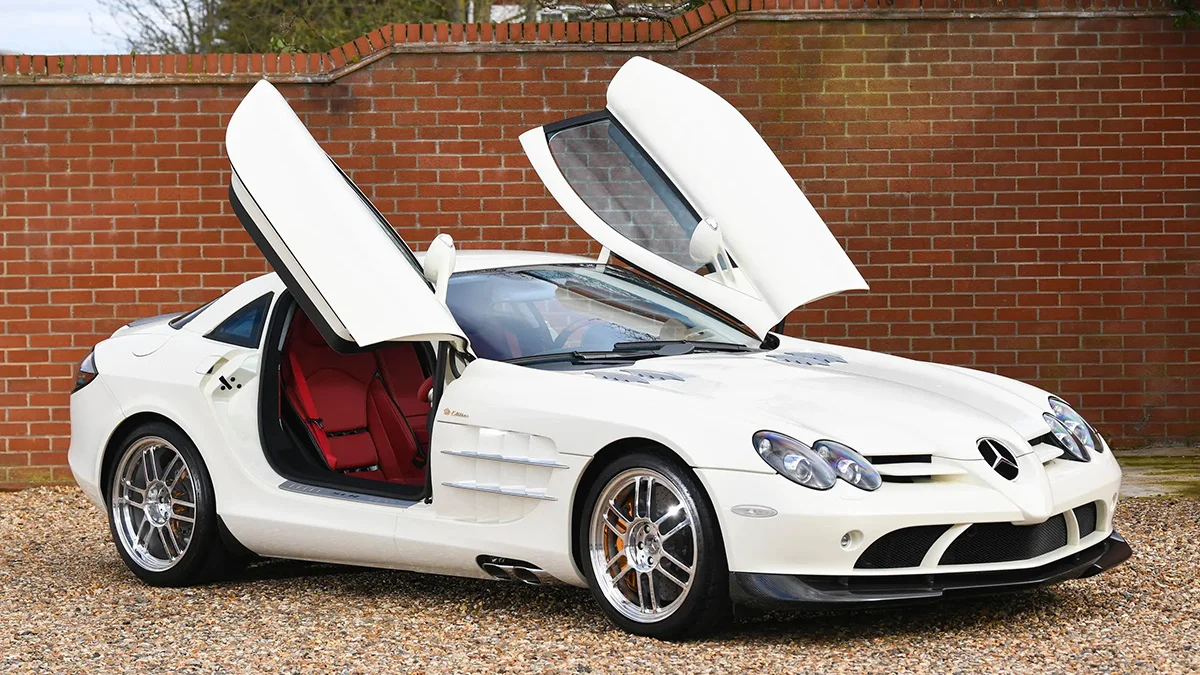 Tranh dán tường siêu xe Mercedes-Benz SLR McLaren màu trắng với cửa cánh chim mở trước tường gạch đỏ
