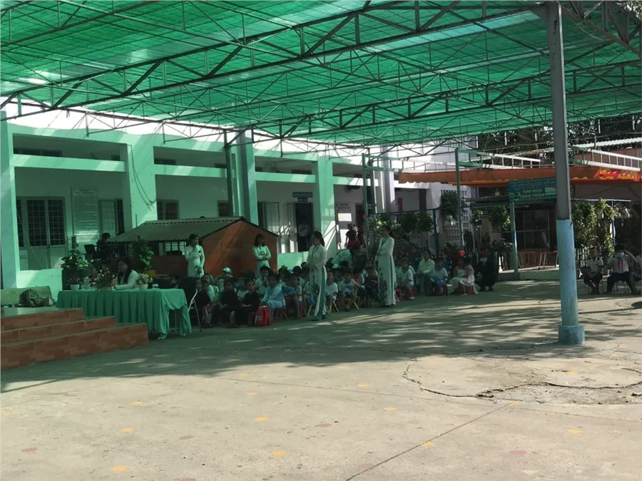 Khu hiên rộng của trường tiểu học với giáo viên và học sinh ngồi dự lễ