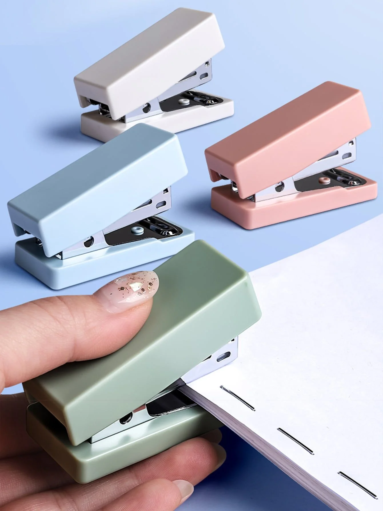 Hình cute chibi bộ dập ghim mini màu pastel xanh, hồng, trắng và xanh sage đang được sử dụng trên giấy
